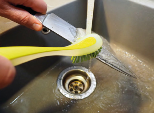 Abb. 17: Reinigen eines Messers mit einer geeigneten Bürste unter fließendem, handwarmen, Wasser.