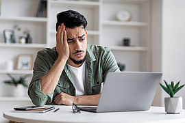 Mann schaut nachdenklich auf seinen Laptop im Homeoffice
