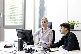 Mitarbeiter spricht mit einer Kollegin an ihrem Bildschirmarbeitsplatz