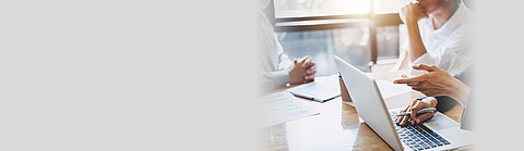 Besprechung mehrerer Personen an einem Tisch auf dem Dokumente liegen und ein Laptop