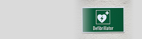 Hinweisschild an der Wand mit Defibrillatorsymbol