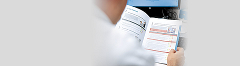 Blick über die Schulter eines Mannes, der eine Broschüre liest.