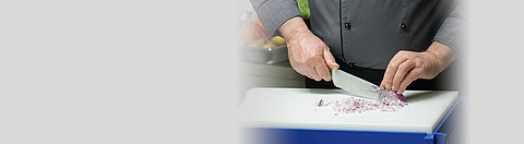 Ein Koch schneidet eine Zwiebel mit einem großen Messer.