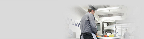 Koch steht an Arbeitstisch und schneidet Gemüse