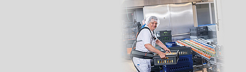 Ein Mitarbeiter hebt eine Kiste und trägt dabei ein Exoskelett.