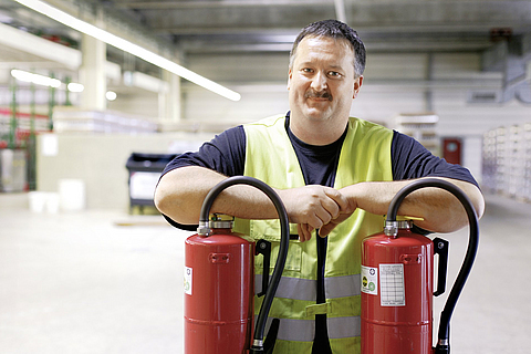 Sicherheitsfachkraft wird mit zwei Feuerlöscher in einer Lagerhalle fotografiert