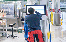 Mitarbeiter steht an einem Bildschirm in einer Abfüllhalle