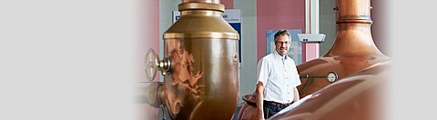 Ein Mann mit weißem Hemd steht zwischen Kupfertanks.