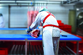 Fleischer zerlegt in gebeugter Haltung ein Fleischstück am Arbeitstisch