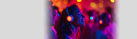 Frau hat Kopfhörer auf und genießt in Menschenmenge die Musik.