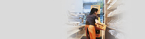 Bäckereimitarbeiterin hebt einen Brotkorb und setzt in um