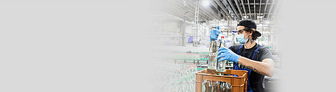 Mitarbeiter setzt Getränkeflaschen in eine Getränkekiste