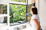 Frau schaut aus weit geöffnetem Fenster.