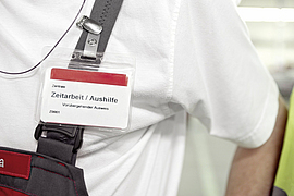 Mann trägt am Träger der Arbeitslatzhose den Ausweis mit der Aufschrift "Zeitarbeit/Aushilfe"