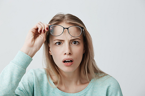 Eine Frau schaut sehr erstaunt und schiebt ihre Brille nach oben, um besser sehen zu können.