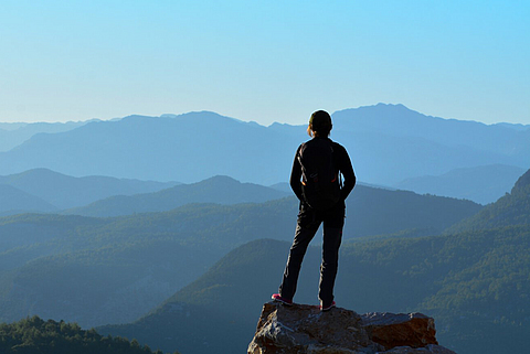 Eine Person steht auf einem Berggipfel und schaut in die Ferne.
