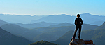 Eine Person steht auf einem Berggipfel und schaut in die Ferne.