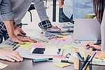 Personen beugen sich über Schreibtisch mit vielen Notizen.