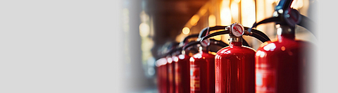 Rote Feuerlöscher stehen aufgereiht in einer dunklen Industriehalle