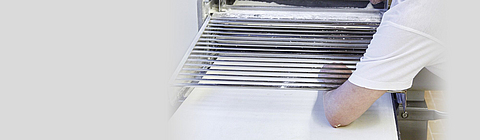 Ein Bäcker streckt seinen Arm in eine Teigausrollmaschine.