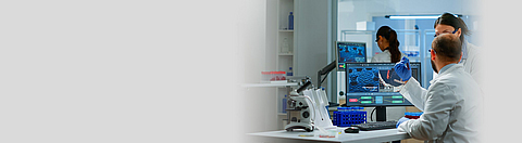 Forscher und Forscherin sitzen am Schreibtisch in einem Labor und arbeiten an Messgeräten.