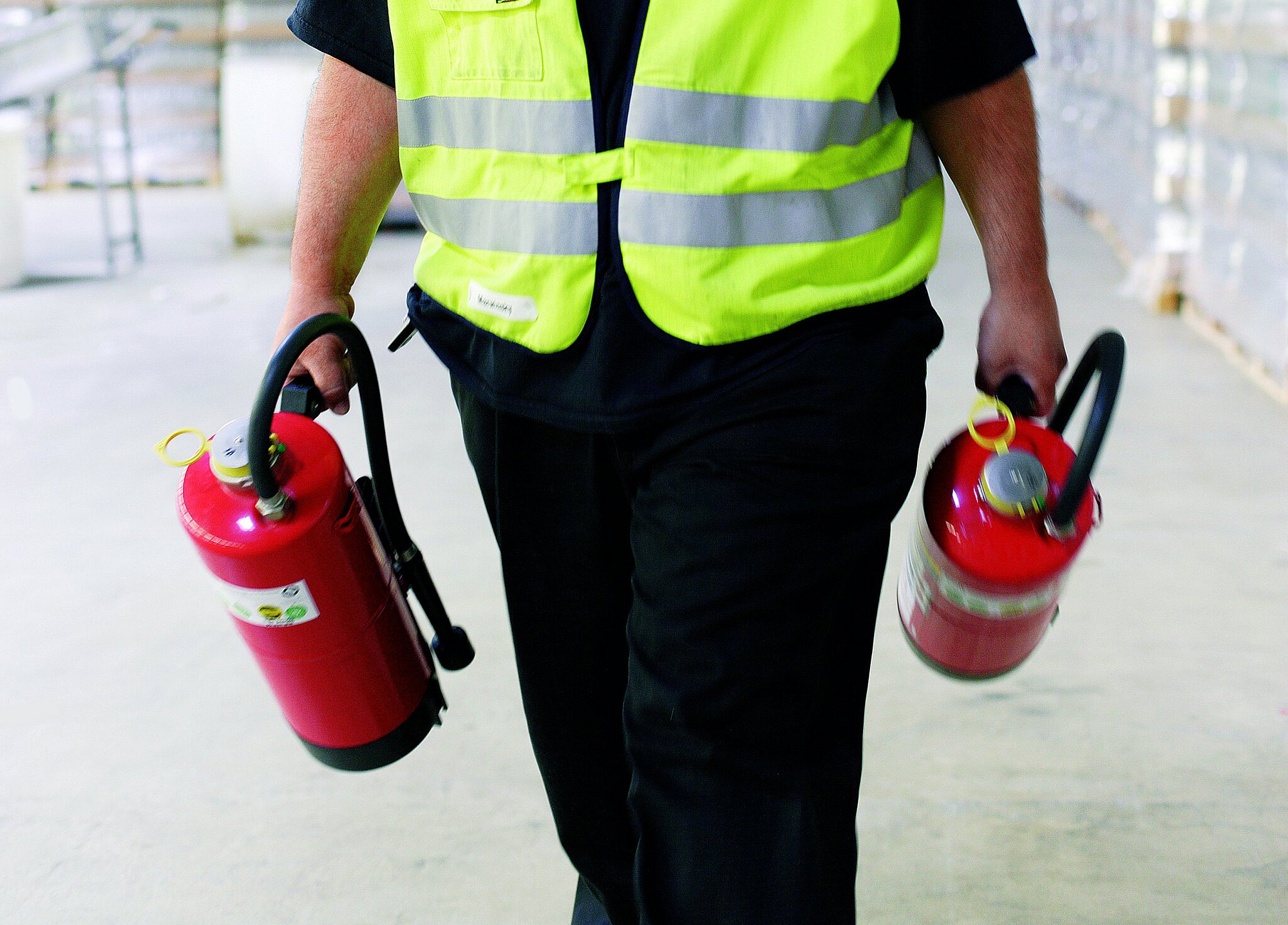 Mitarbeiter trägt Feuerlöscher in je einer Hand