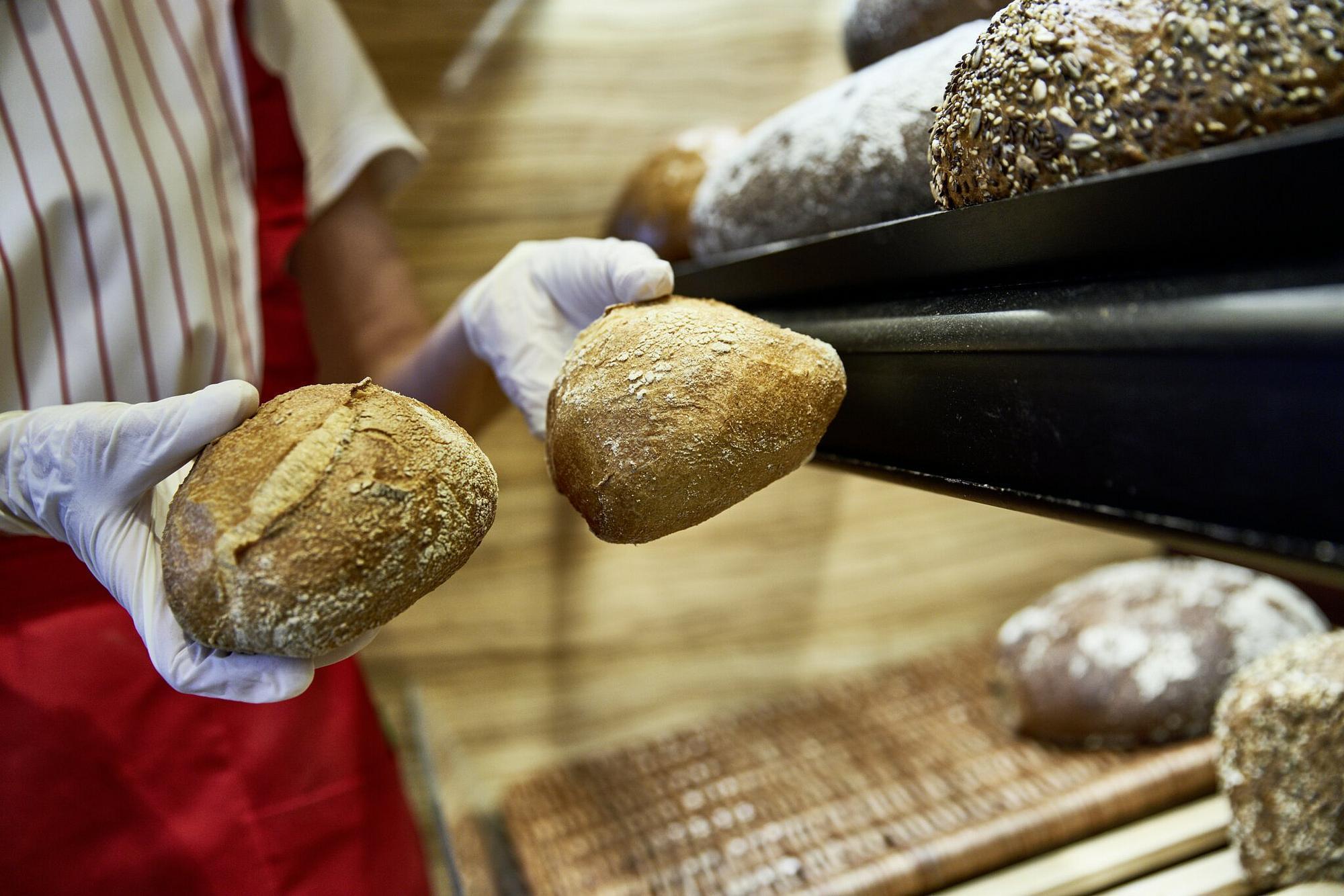 Bäckereivrekäuferin trägt Handschuhe beim Brötcheneinpacken