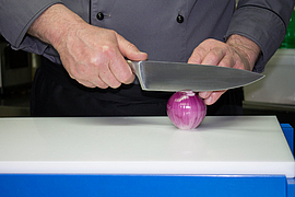 Koch schneidet rote Zwiebel zur Hälfte auf Schneidebretterhöhung