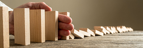 Hand stoppt umfallende Dominosteine