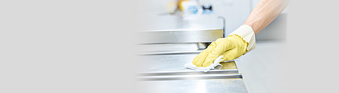Person trägt Schutzhandschuh und putzt dabei eine Edelstahloberfläche.