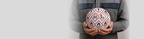 Person hält einen Ball mit Gefahrstoffsymbolen darauf in den Händen