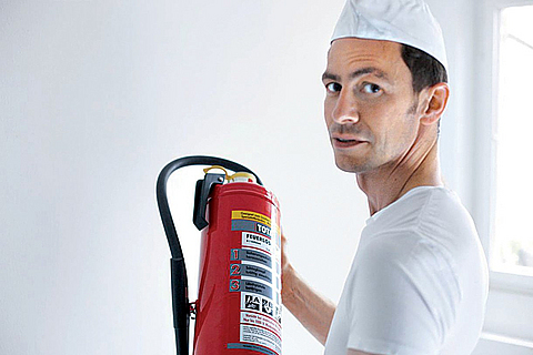 Mann hat einen Feuerlöscher in der Hand und schaut in die Kamera