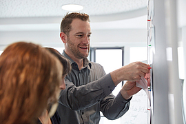 Ein Mitarbeiter macht bei einer Besprechung einen Zettel an eine Pinnwand.