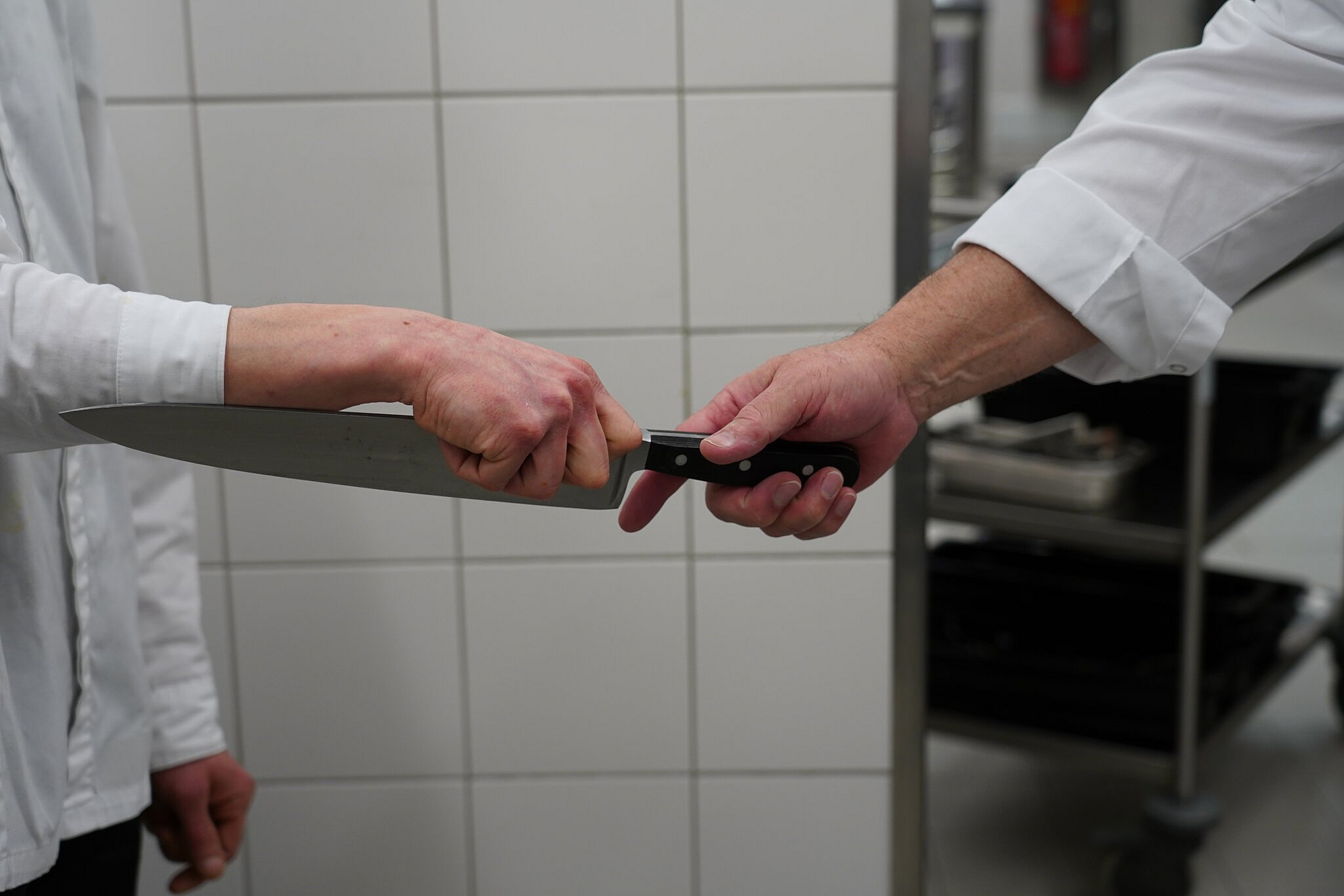 Ein Koch übergibt dem anderen auf sicherem Weg ein Messer zum Arbeiten.