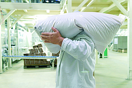 Mitarbeiter trägt einen Sack Rohstoff auf der Schulter