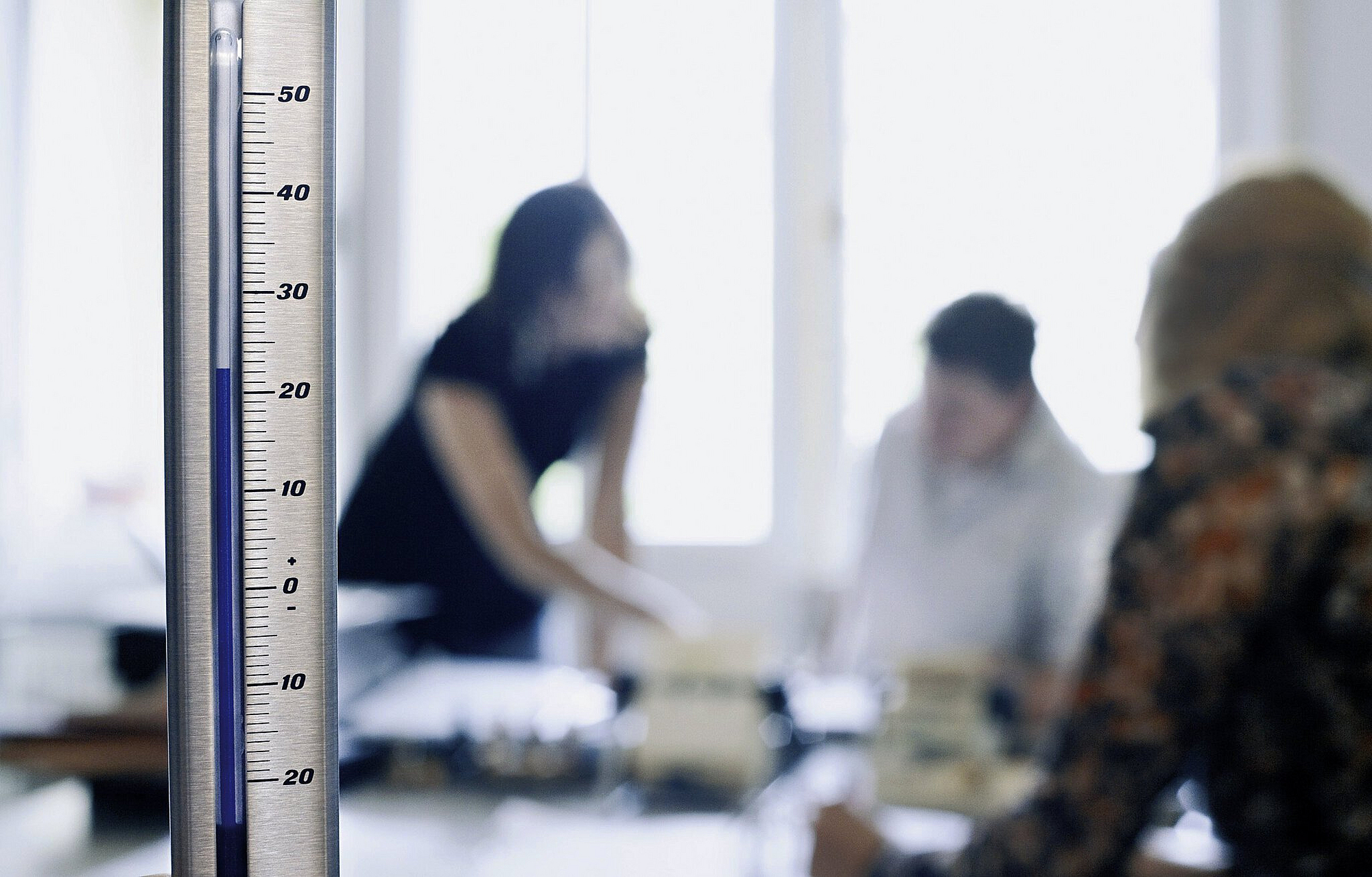 Büro mit 3 Personen, im Vordergrund Thermometer, das 22 Grad Celsius anzeigt