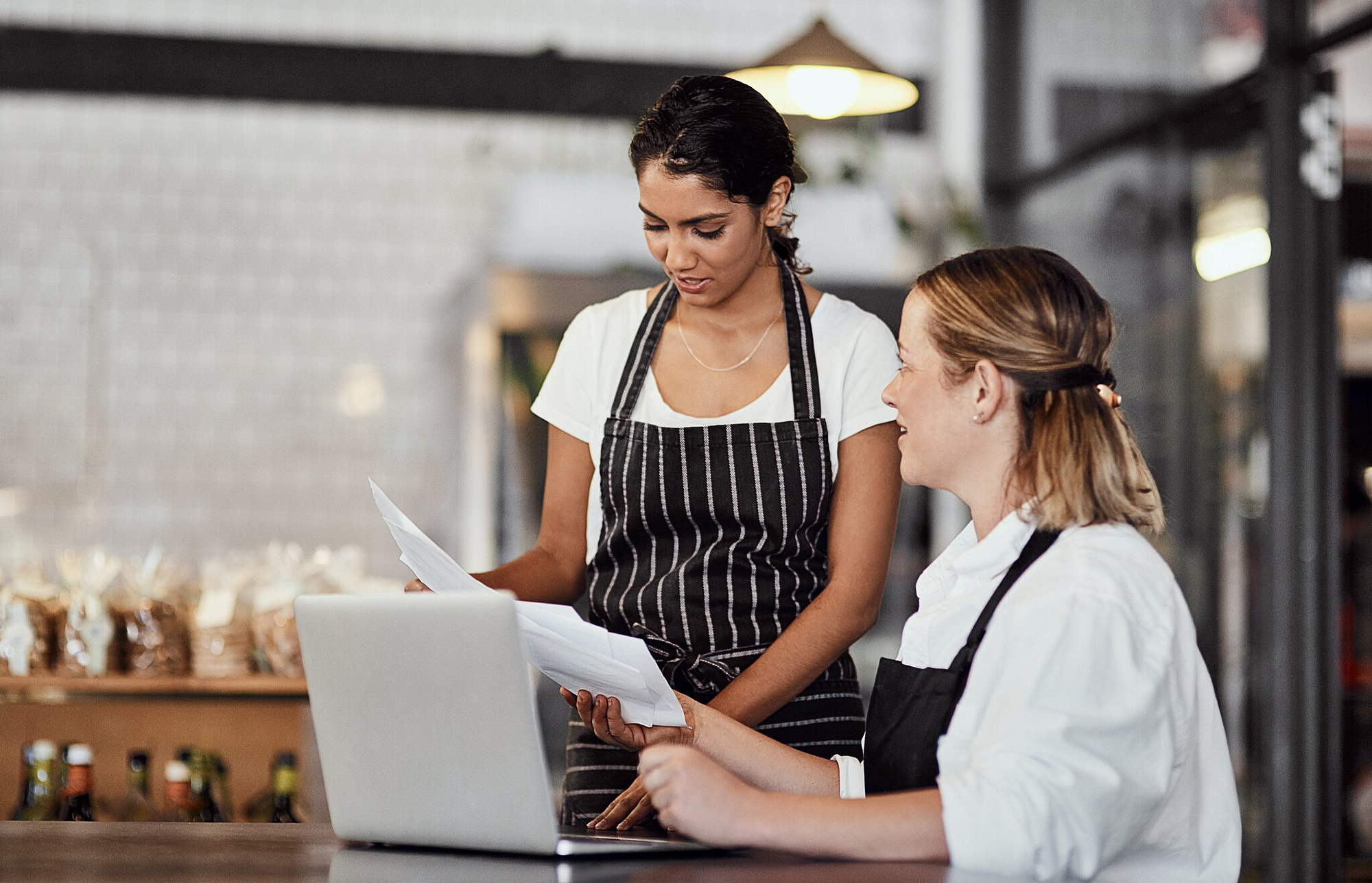 In einem Restaurant bespreche zwei Mitarbeiterinnen mit Papierkram und Laptop Themen.