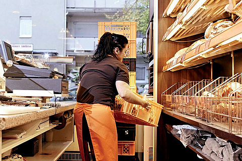 Bäckereifachverkäuferin hebt eine Kiste mit Backwaren hoch