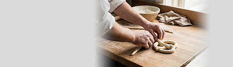 Bäcker formt rohen Teig zu einer Brezel auf einer Holzarbeitsplatte