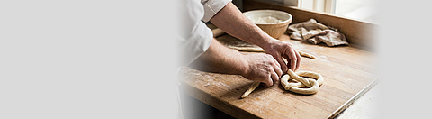 Bäcker formt rohen Teig zu einer Brezel auf einer Holzarbeitsplatte