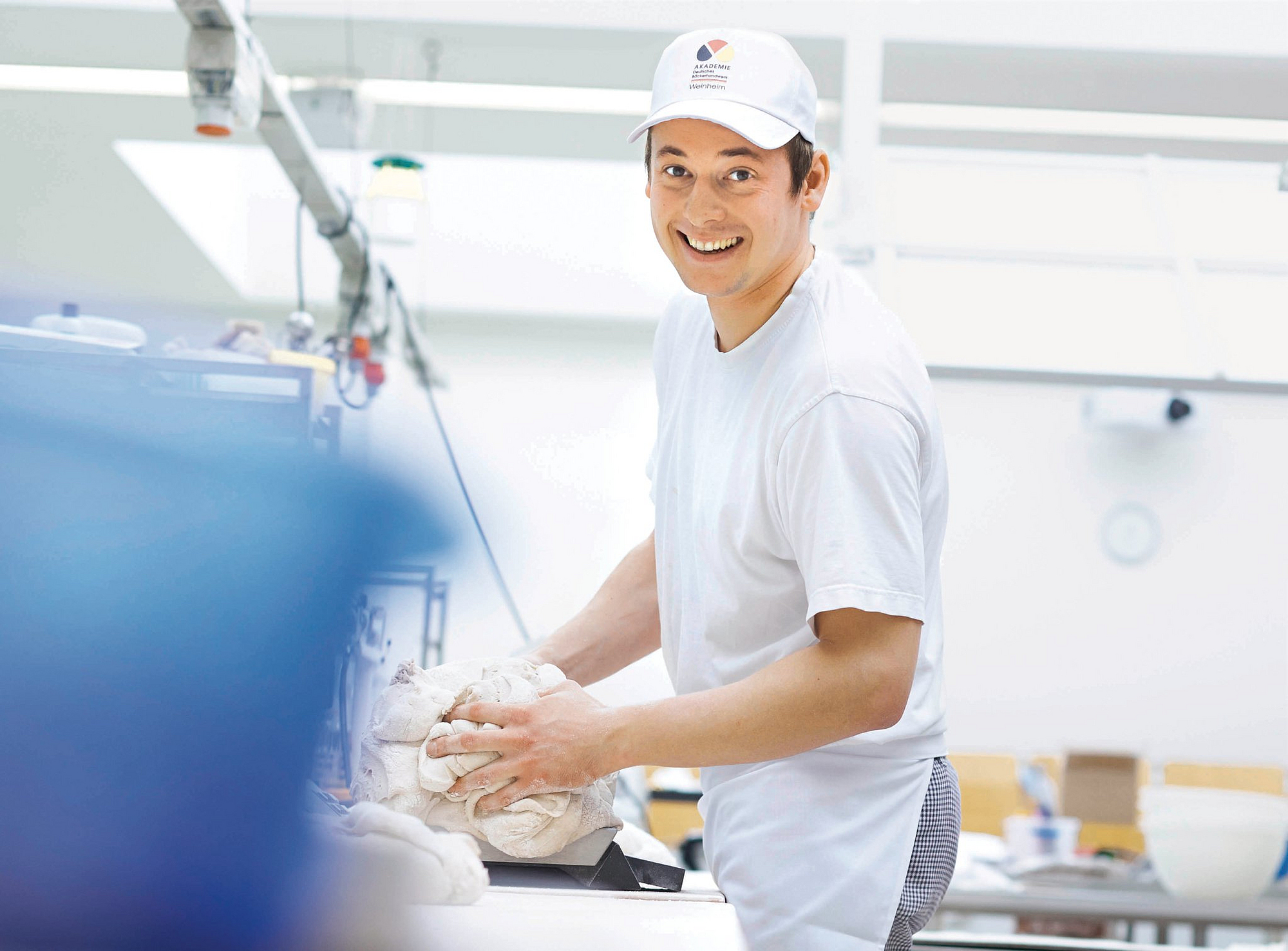 Junger Bäcker knetet Teig und lächelt in die Kamera