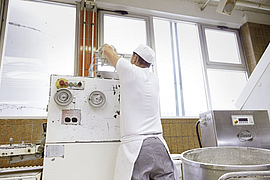 Bäcker wirft über Kopf Teigklumpen in den   Trichter eines Teigteilers                                              Trichter eines Teigteilers