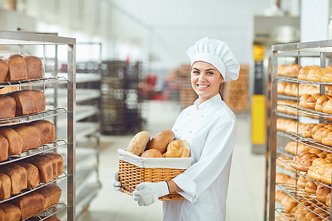 Bäckerin  mit einem Korb voller Brötchen in einer Bäckerei.