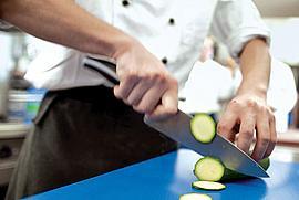 Koch schneidet mit einem großen Messer eine Gurke in Scheiben