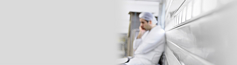 Erschöpfter Mitarbeiter sitzt in Produktionshalle und hält sich den Kopf