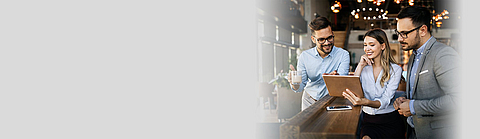 Zwei Männer und eine Frau stehen an einer Theke und schauen auf ein Tablet.