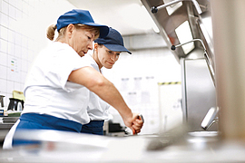 Praktikantin schaut Köchin bei der Arbeit zu