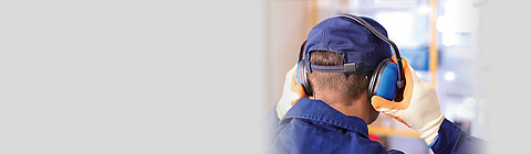 Ein Mann von hinten, der sich einen Gehörschutz aufsetzt.