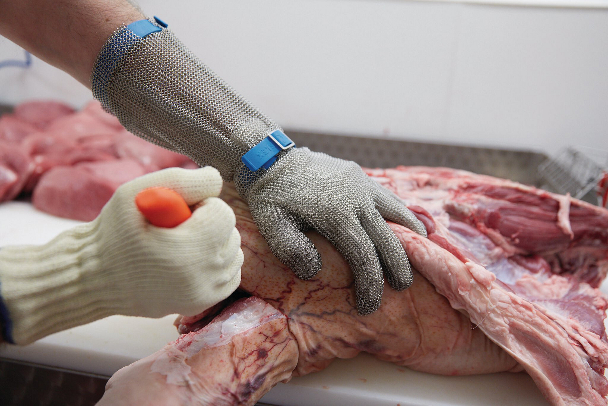 Ausbeinarbeit mit Schnittschutzhandschuh an Messer führender Hand und Stechschutzhandschuh an der anderen Hand