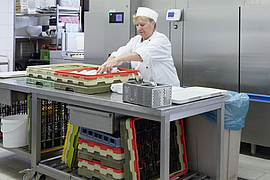 Mitarbeiterin in Spülküche hebt Tassen aus einem Rack